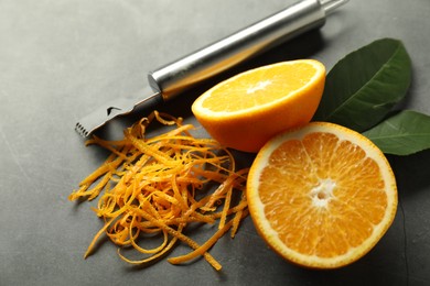 Photo of Orange zest, zester tool and fresh fruit pieces on gray textured table, closeup