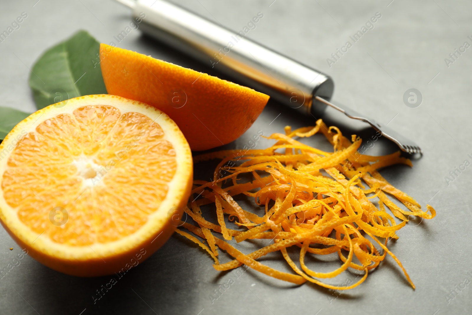 Photo of Orange zest, zester tool and fresh fruit pieces on gray textured table, closeup