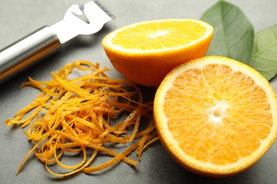 Photo of Orange zest, zester tool and fresh fruit pieces on gray textured table, closeup