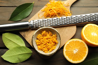 Photo of Orange zest, grater and fresh fruit pieces on wooden table, flat lay