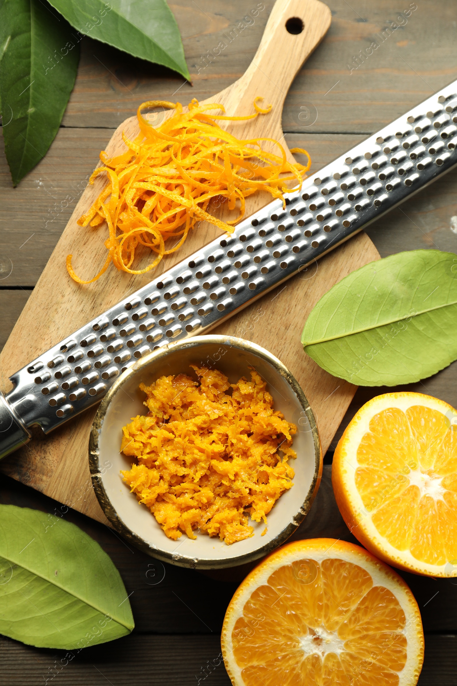 Photo of Orange zest, grater and fresh fruit pieces on wooden table, flat lay