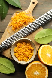 Photo of Orange zest, grater and fresh fruit pieces on wooden table, flat lay