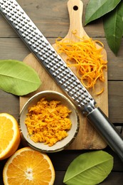 Photo of Orange zest, grater and fresh fruit pieces on wooden table, flat lay