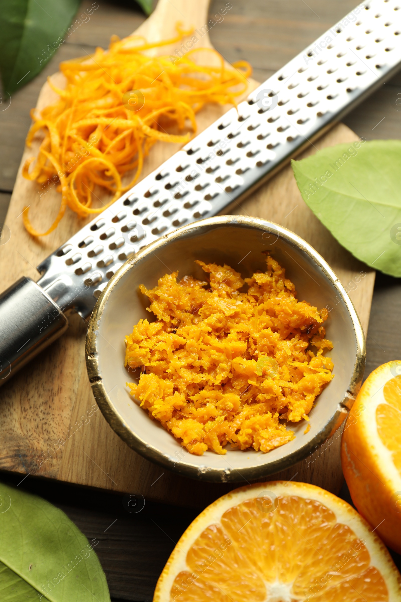 Photo of Orange zest, grater and fresh fruit pieces on wooden table, flat lay