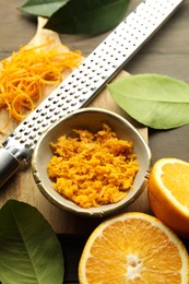 Photo of Orange zest, grater and fresh fruit pieces on wooden table, flat lay