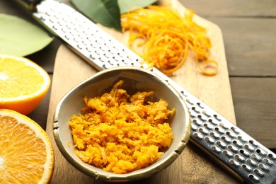 Photo of Orange zest, grater and fresh fruit pieces on wooden table, closeup