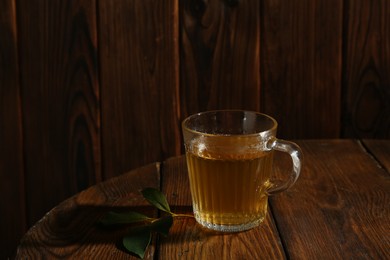 Refreshing green tea in cup and leaves on wooden table. Space for text