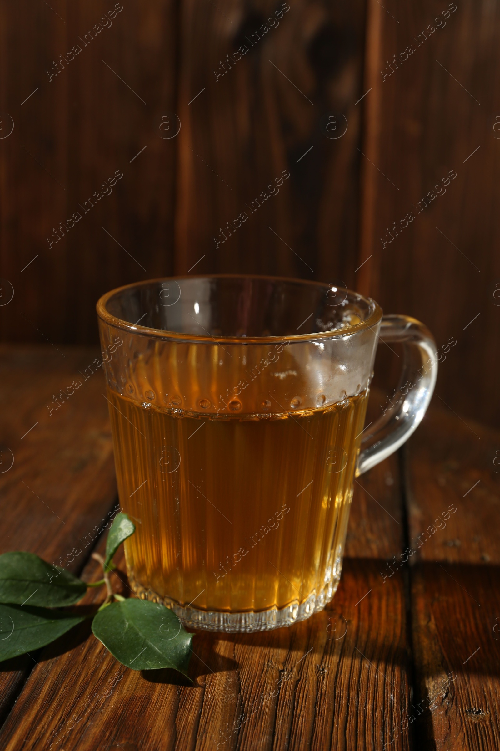 Photo of Refreshing green tea in cup and leaves on wooden table, closeup