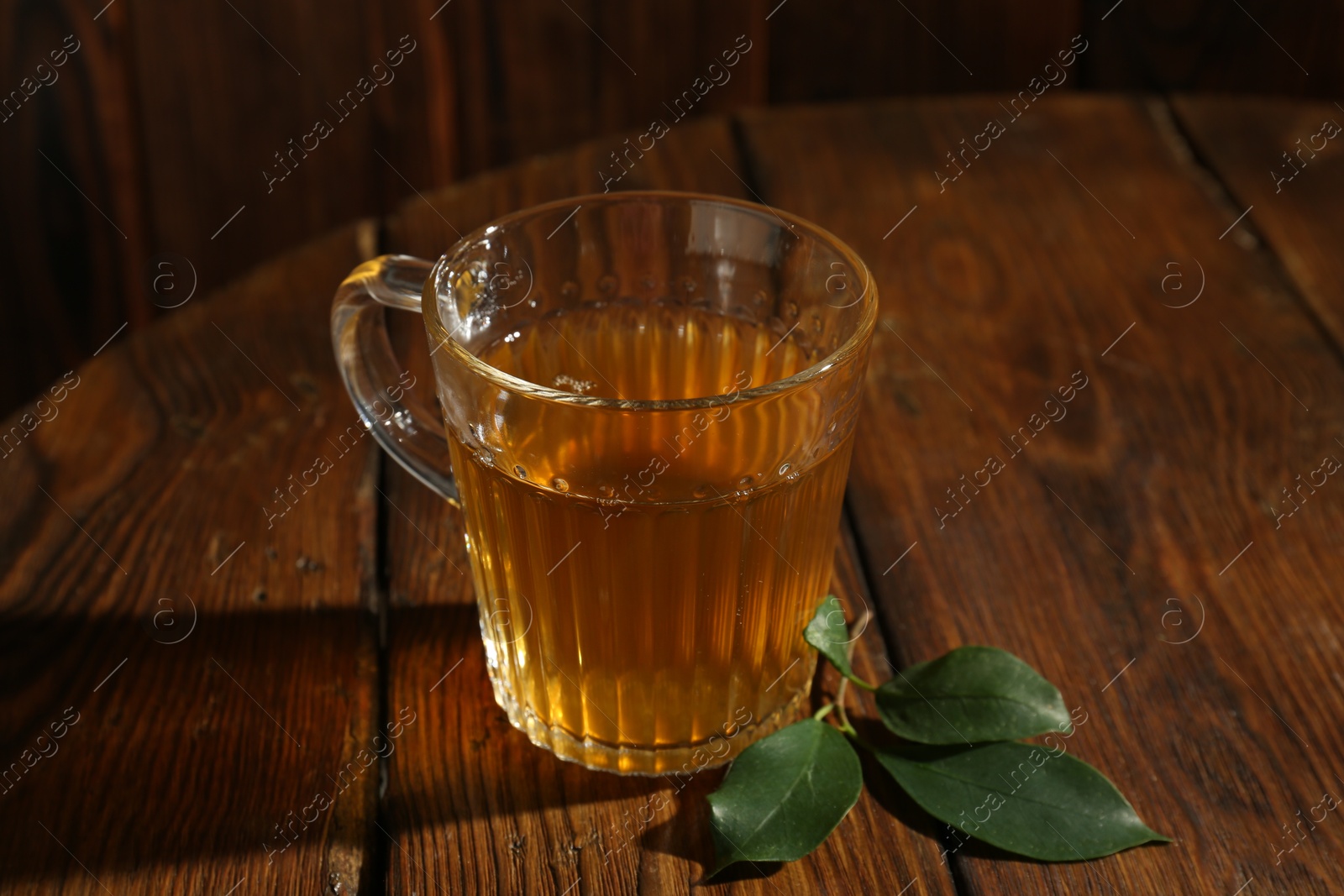 Photo of Refreshing green tea in cup and leaves on wooden table, closeup