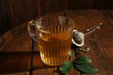 Photo of Refreshing green tea in cup and leaves on wooden table, closeup