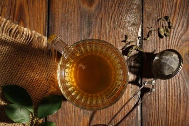 Photo of Refreshing green tea in cup, strainer and leaves on wooden table, flat lay