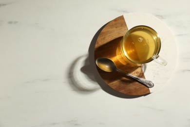 Photo of Refreshing green tea in cup and spoon on white marble table, top view. Space for text