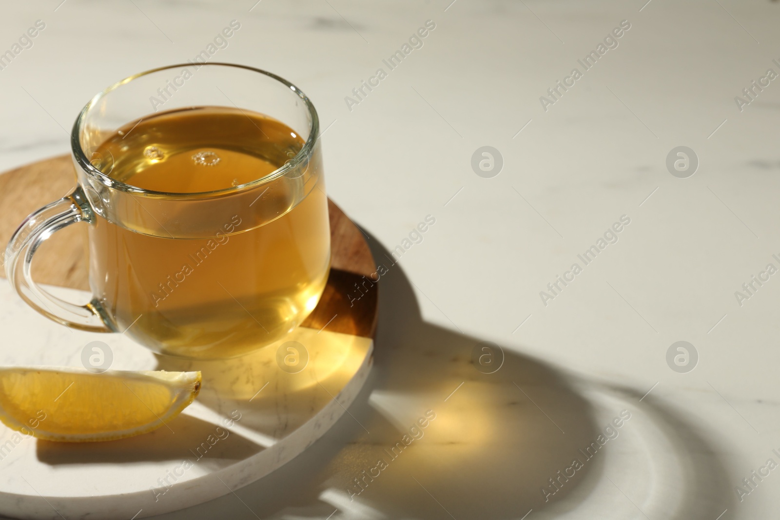 Photo of Refreshing green tea in cup and slice of lemon on white marble table, closeup. Space for text