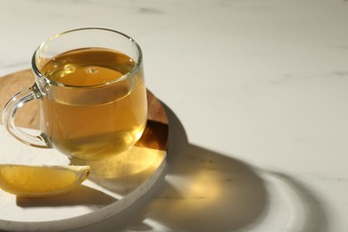 Photo of Refreshing green tea in cup and slice of lemon on white marble table, closeup. Space for text