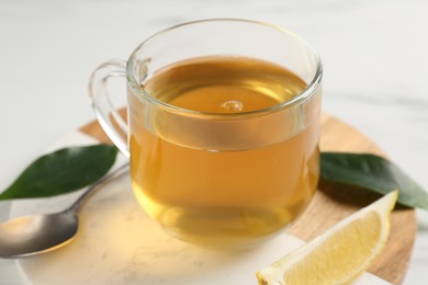 Photo of Refreshing green tea in cup, spoon and slice of lemon on white table, closeup