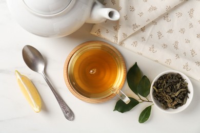 Photo of Refreshing green tea in cup, spoon, leaves and slice of lemon on white table, flat lay