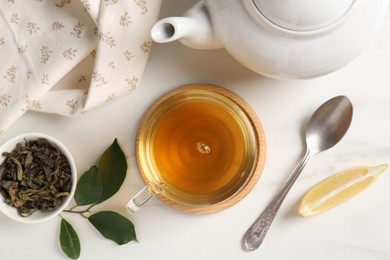 Photo of Refreshing green tea in cup, spoon, leaves and slice of lemon on white table, flat lay