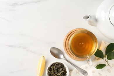 Refreshing green tea in cup, spoon, leaves and slice of lemon on white marble table, flat lay. Space for text