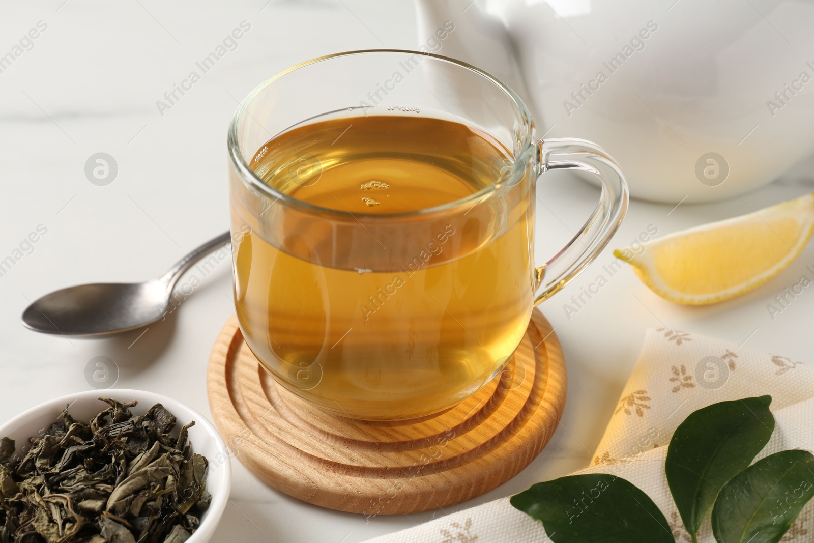 Photo of Refreshing green tea in cup and leaves on white table, closeup