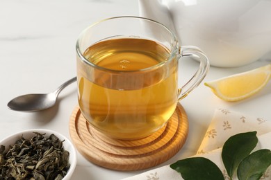 Photo of Refreshing green tea in cup and leaves on white table, closeup