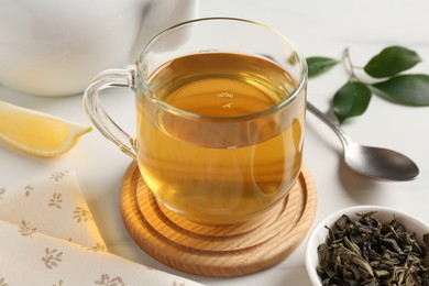 Photo of Refreshing green tea in cup and leaves on white table, closeup