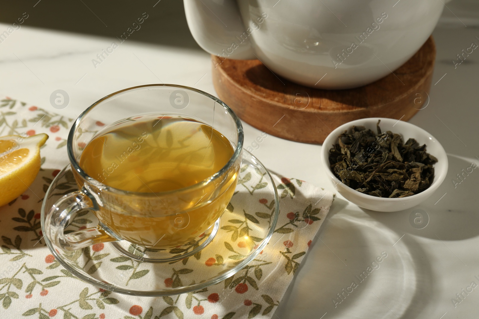 Photo of Refreshing green tea in cup and dry leaves on white table, closeup