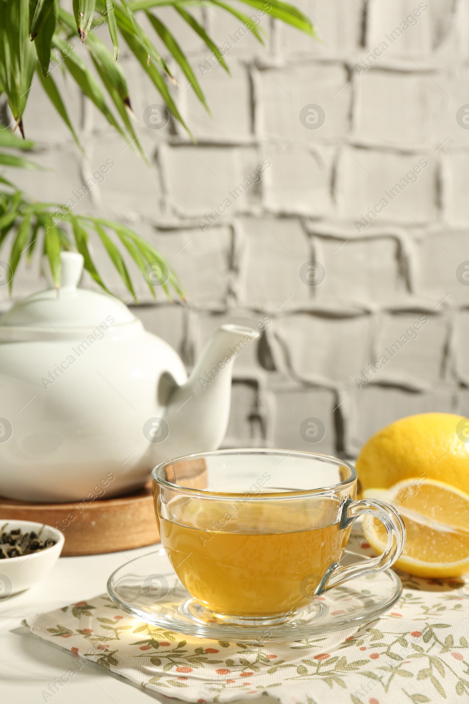 Photo of Refreshing green tea in cup, lemon and dry leaves on white table against grey textured wall