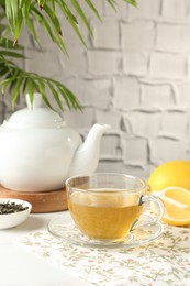 Photo of Refreshing green tea in cup, lemon and dry leaves on white table against grey textured wall