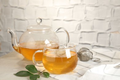 Photo of Refreshing green tea, strainer and leaves on light table against textured wall, closeup