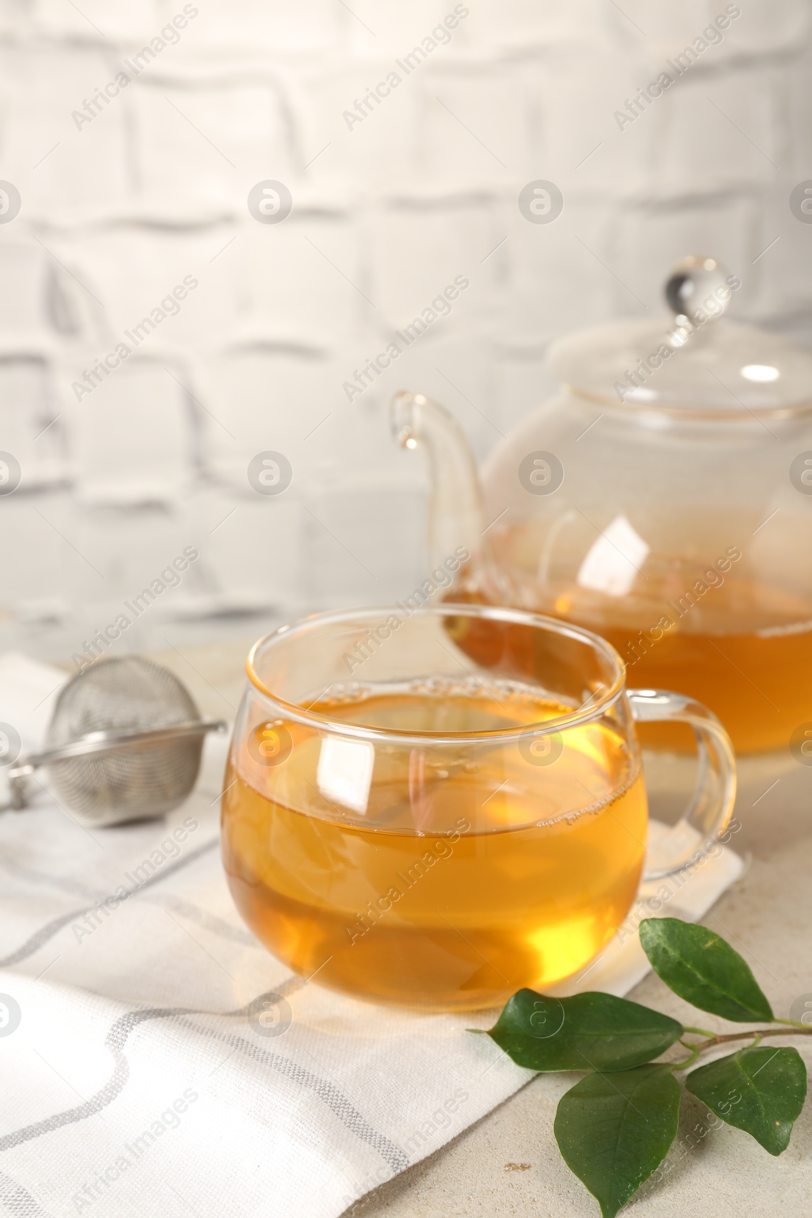 Photo of Refreshing green tea, strainer and leaves on light table against textured wall, closeup