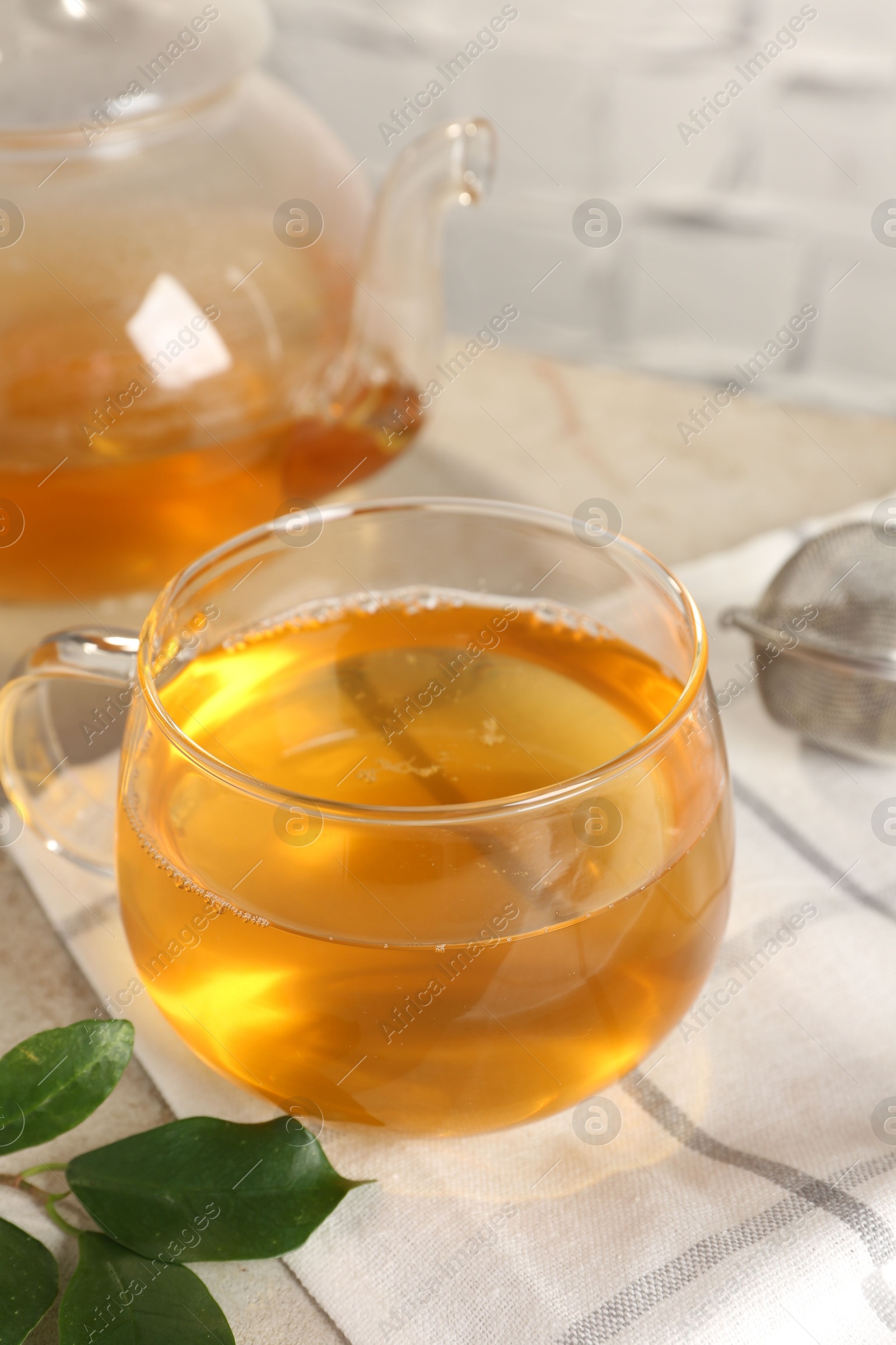 Photo of Refreshing green tea in cup, strainer and leaves on table, closeup