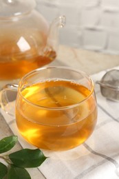 Photo of Refreshing green tea in cup, strainer and leaves on table, closeup