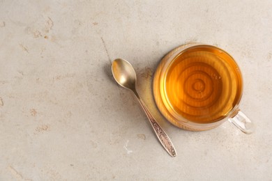 Photo of Refreshing green tea in cup and spoon on light textured table, top view. Space for text