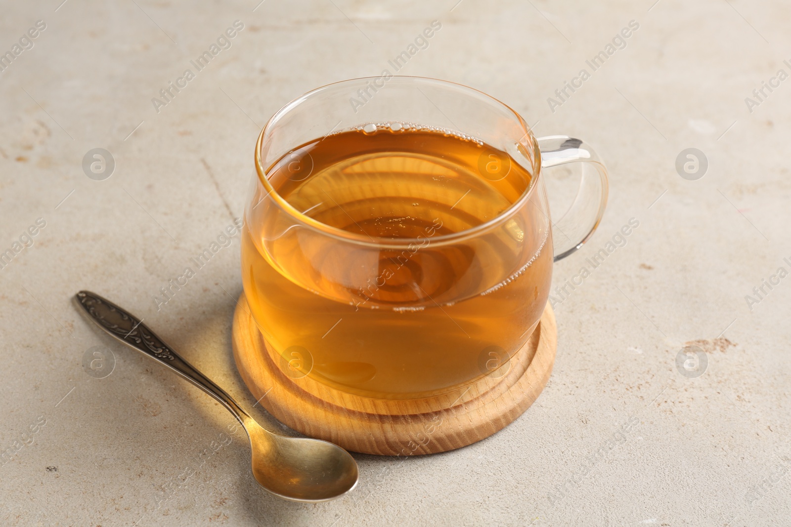 Photo of Refreshing green tea in cup and spoon on light textured table, closeup