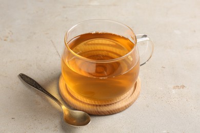 Photo of Refreshing green tea in cup and spoon on light textured table, closeup