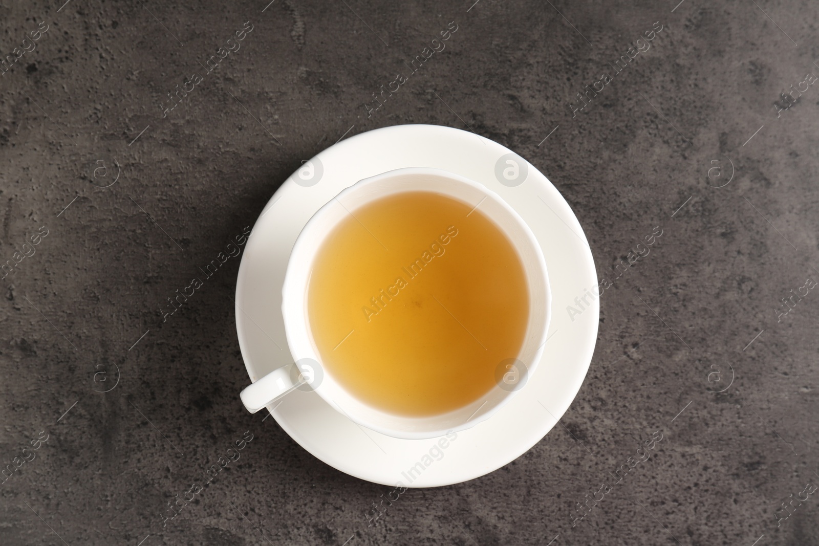 Photo of Refreshing green tea in cup on grey textured table, top view