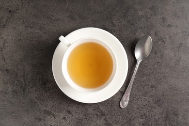 Photo of Refreshing green tea in cup and spoon on grey textured table, top view