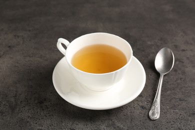 Photo of Refreshing green tea in cup and spoon on grey textured table, closeup