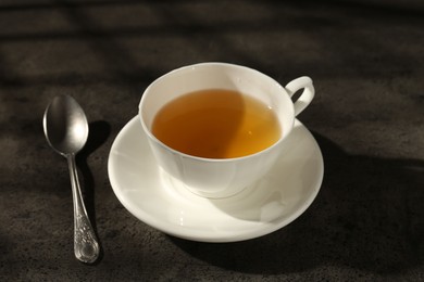 Photo of Refreshing green tea in cup and spoon on dark textured table, closeup