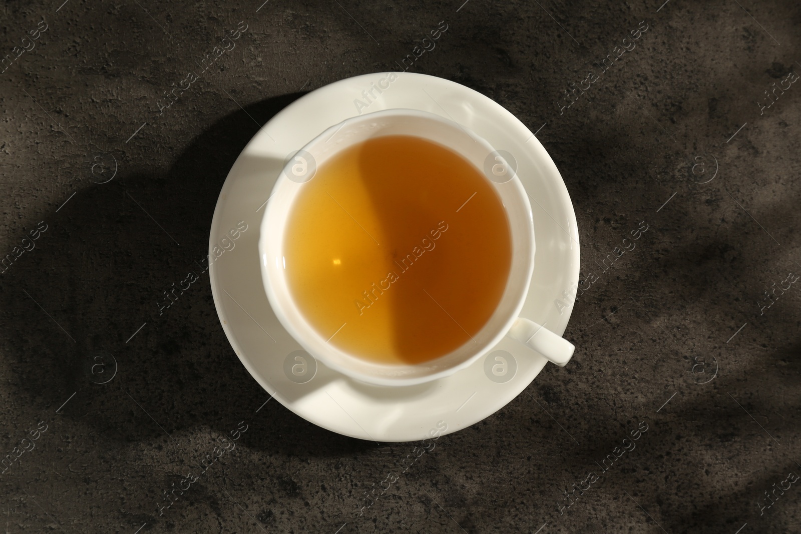 Photo of Refreshing green tea in cup on dark textured table, top view