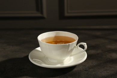 Photo of Refreshing green tea in cup on dark textured table, closeup