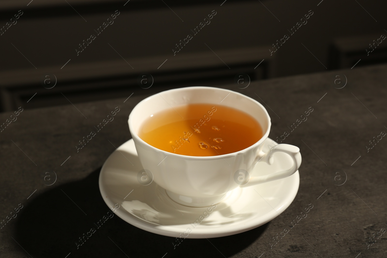 Photo of Refreshing green tea in cup on dark textured table, closeup