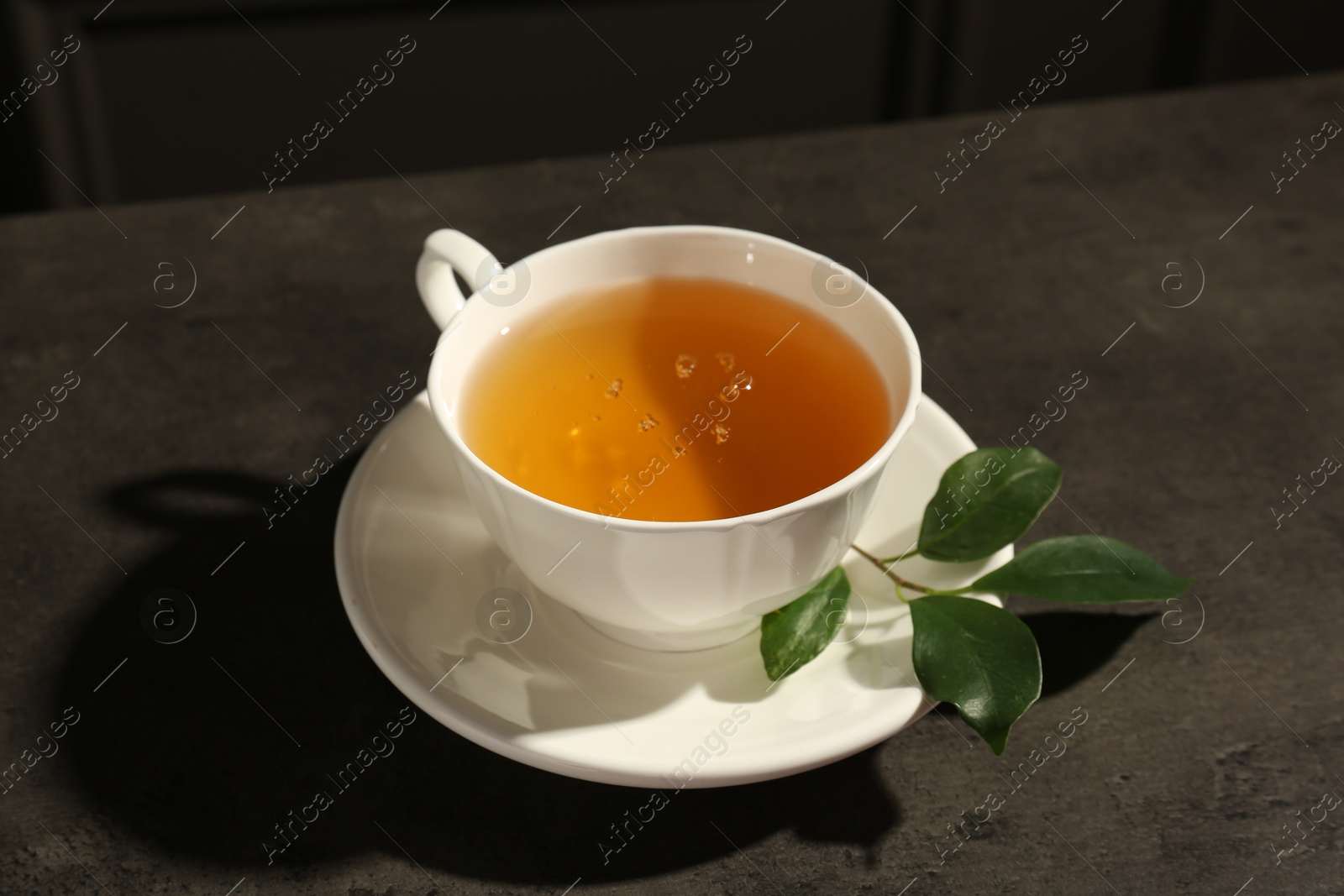 Photo of Refreshing green tea in cup and leaves on dark textured table, closeup