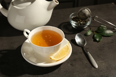 Photo of Refreshing green tea in cup and slice of lemon on dark textured table