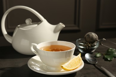 Photo of Refreshing green tea in cup and slice of lemon on dark textured table