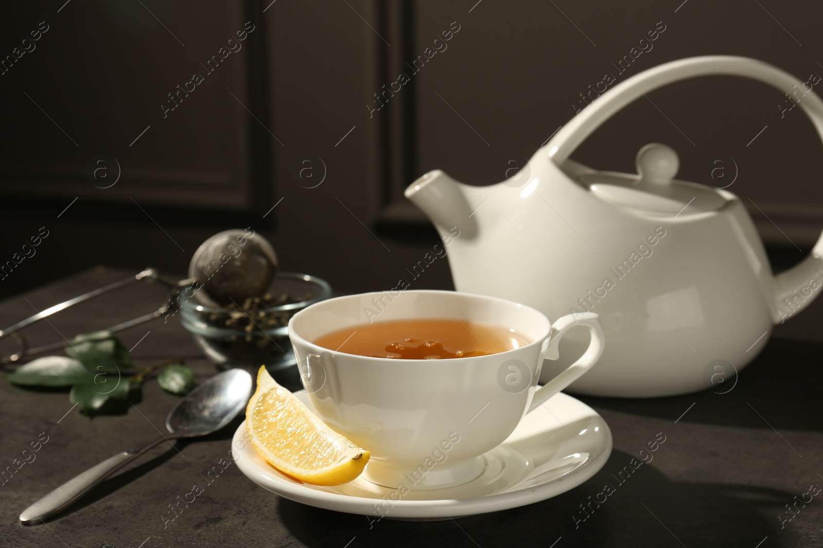 Photo of Refreshing green tea in cup and slice of lemon on dark textured table