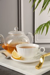 Photo of Refreshing green tea, spoon and slice of lemon on dark textured table