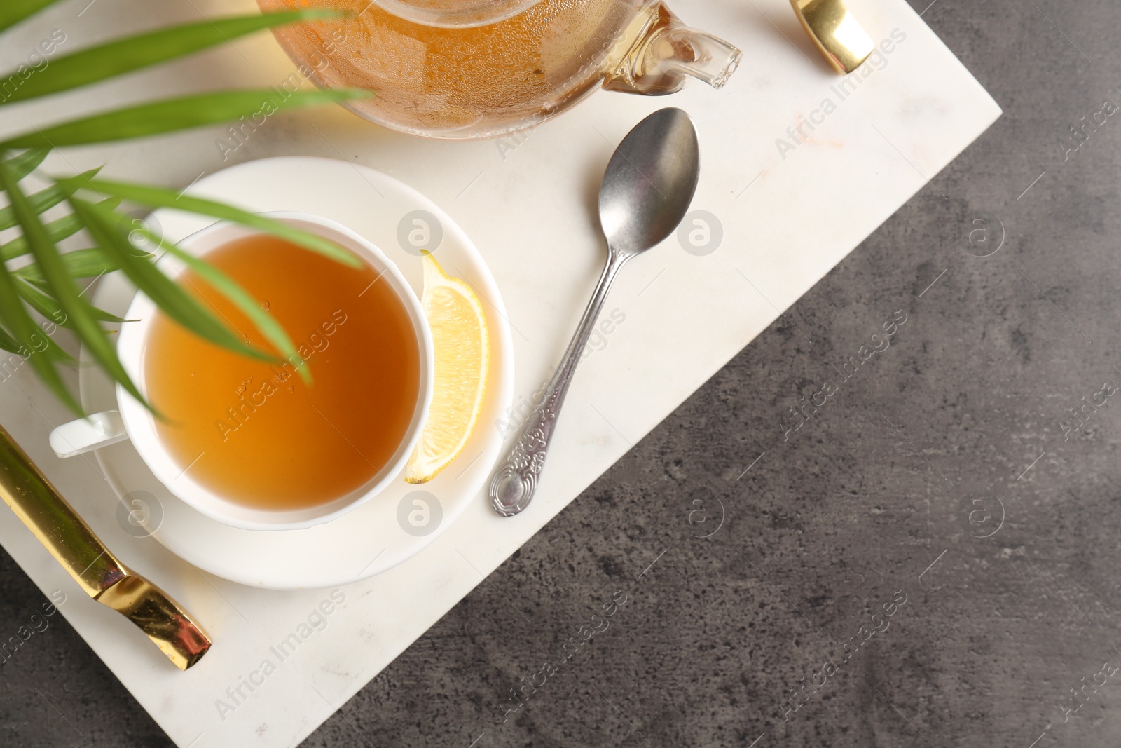 Photo of Refreshing green tea, spoon and slice of lemon served on dark textured table, top view. Space for text