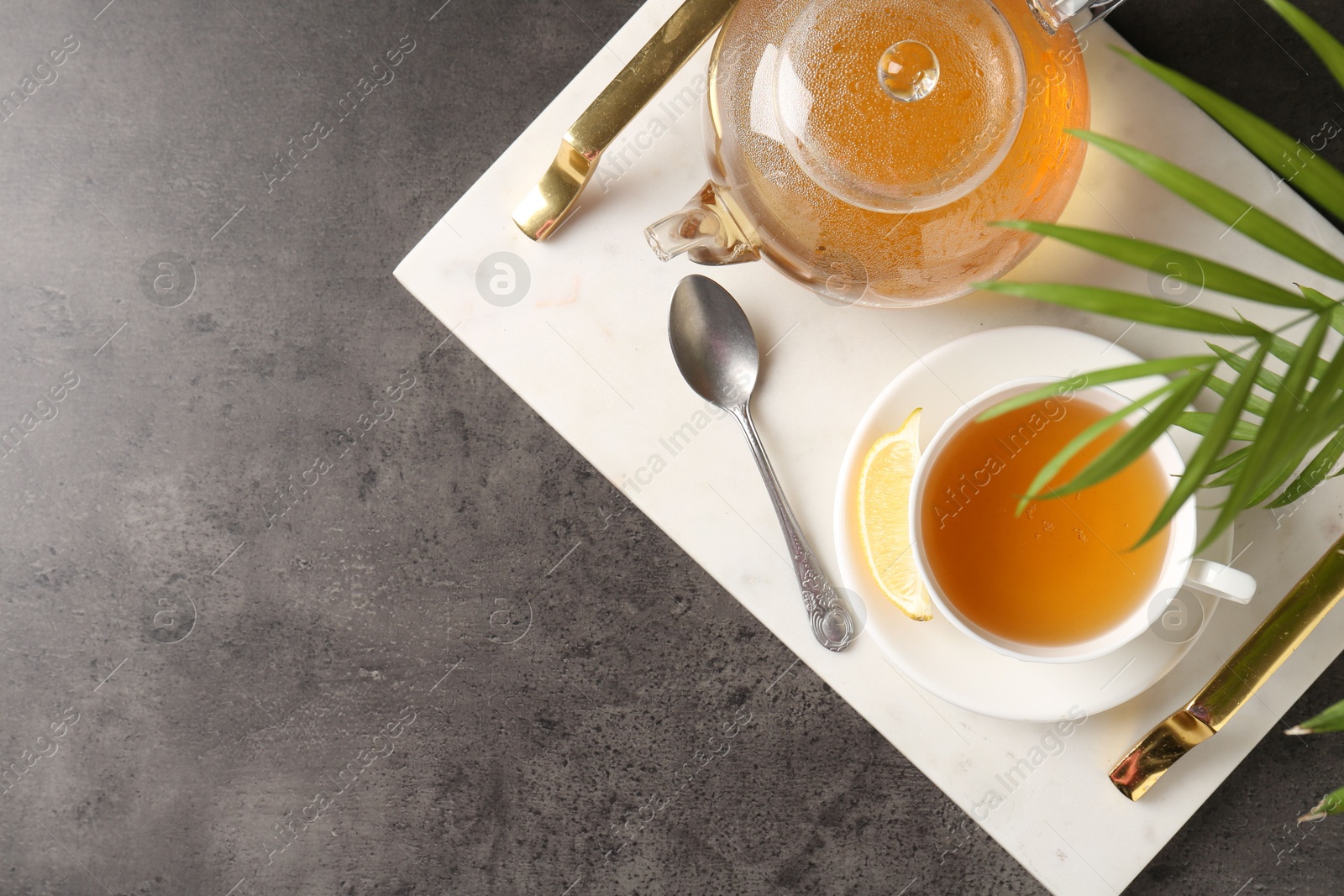 Photo of Refreshing green tea, spoon and slice of lemon served on dark textured table, top view. Space for text