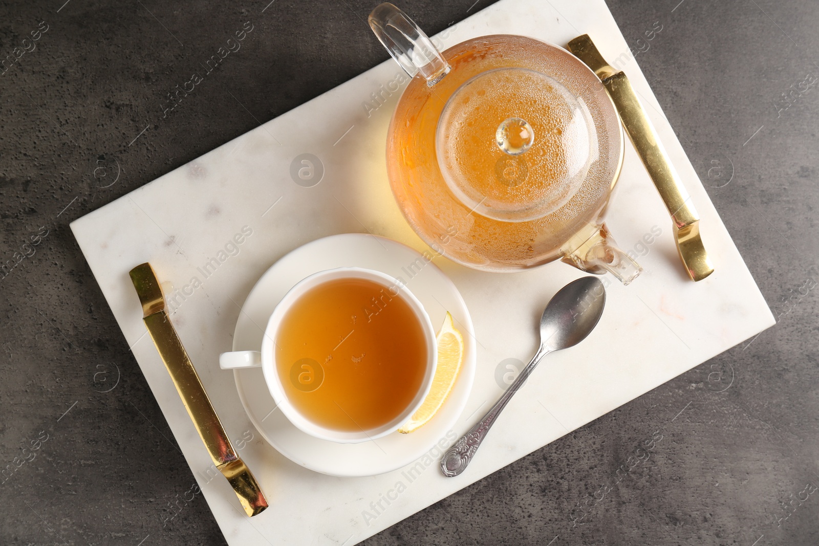 Photo of Refreshing green tea, spoon and slice of lemon served on dark textured table, top view